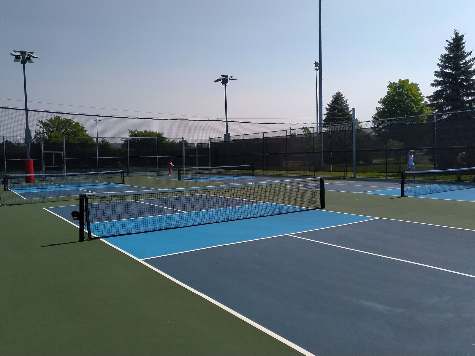 Outdoor pickleball courts with blue surfaces under tall lights at dusk