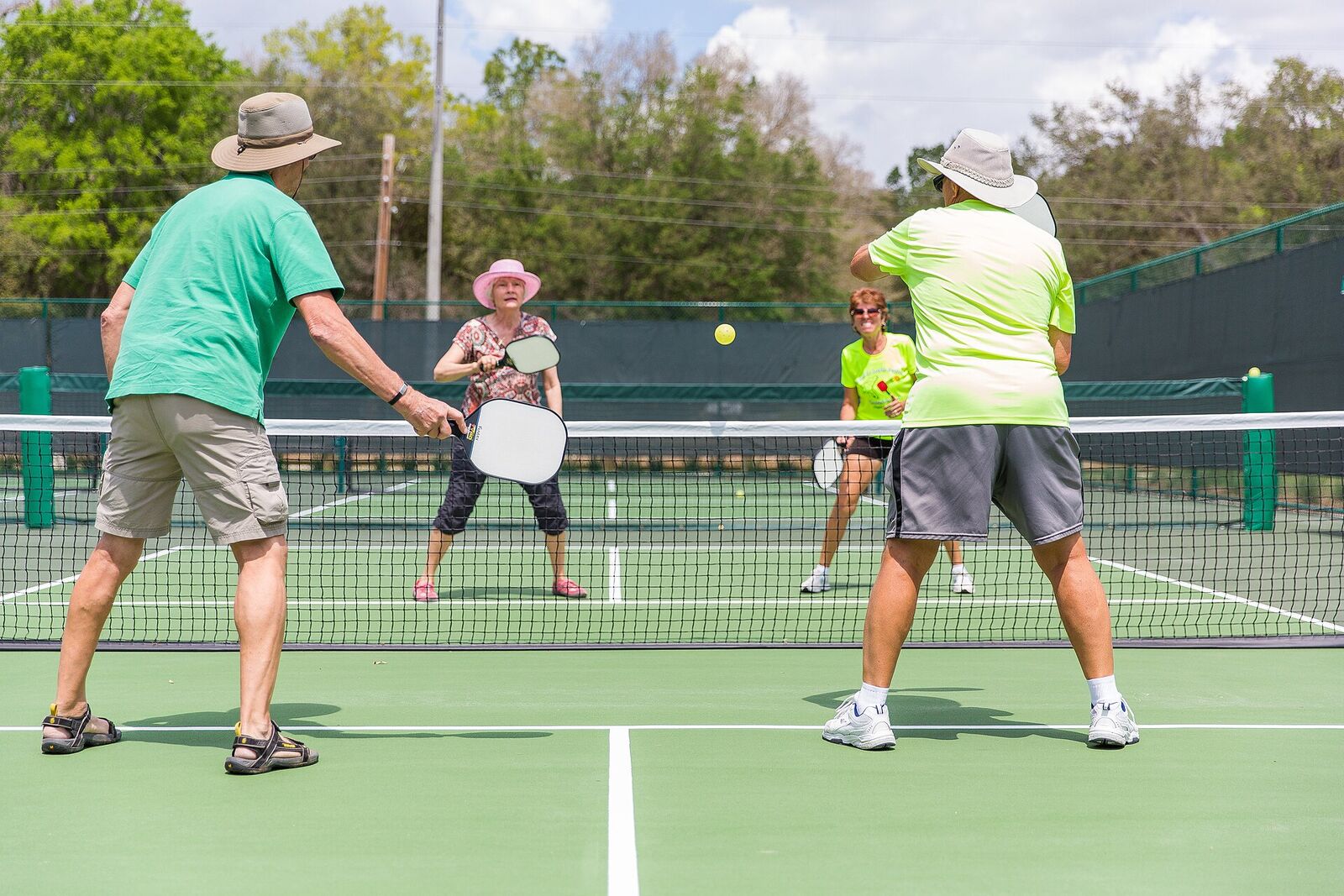 Four players in a doubles game at the net on a green outdoor court