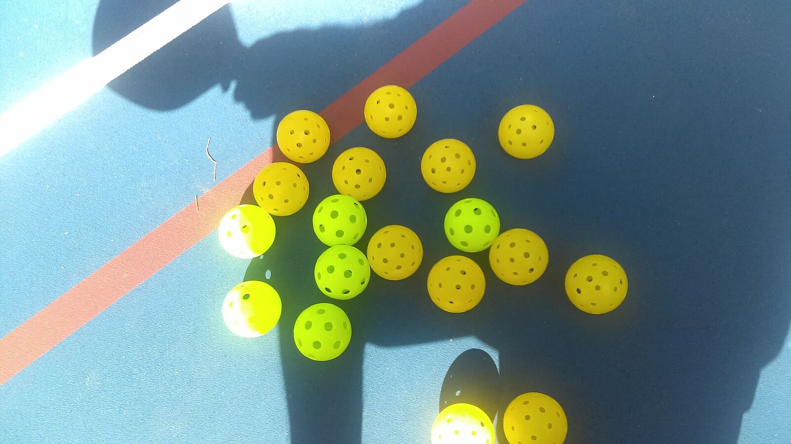 Yellow and green pickleballs scattered on a blue court in low sun