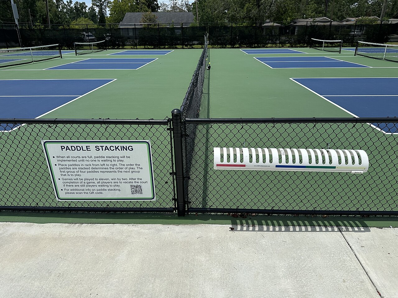 A paddle-stacking rack on the fence between courts, where open-play players queue for the next game