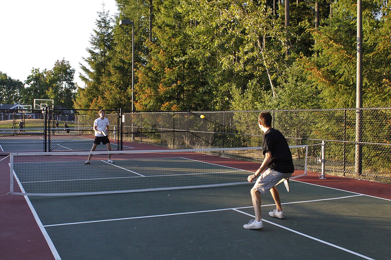 Two players in a singles match on a red and green outdoor court